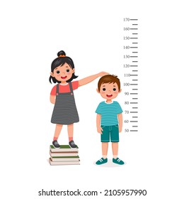 cute little girl standing on stack of books measuring height of little boy growth with measurement ruler on the background of wall