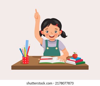 Cute little girl student rising hand answering question sitting at her desk in the classroom