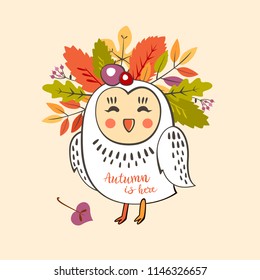 a cute owl with a wreath of autumn leaves and berries on his head with the inscription autumn is here and the leaf