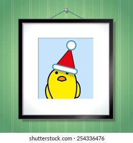 Cute Portrait of Single Yellow Chick Wearing Santa Hat in Picture Frame Hanging on Green Wallpaper Background