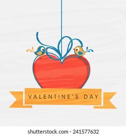 Cute romantic love bird sitting on red hanging heart with text on ribbon for Happy Valentine's Day celebration on white background.