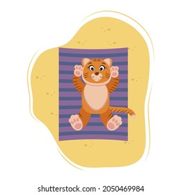 cute tiger lies and basks on the sand, on the beach, on a striped towel