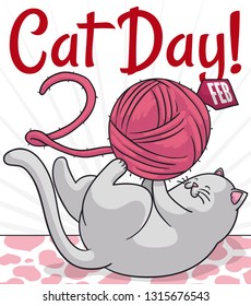 Cute white cat lying in the floor with heart pattern, playing with its string ball and forming the date for the Cat Day celebration: February 20.