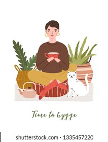 Cute young woman drinking tea, cat, houseplants and Time To Hygge slogan handwritten with cursive font. Comfortable house or apartment decorated in cozy Scandic style. Flat vector illustration.