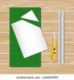 Cutter, ruler, paper and green cutting mat on wooden background. Vector stationery object set.