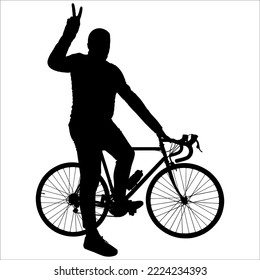 The cyclist poses for the camera. The man and the bicycle are sideways. The guy is standing near the bike, holding the steering wheel with one hand; the second hand shows the gesture of "victory".