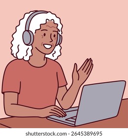 Dark skinned young woman with curly hair wears headphones and waves while communicating remotely via laptop in online meeting