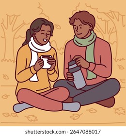 Dark-skinned couple dressed in warm clothes sits on ground in autumn park, drinking hot beverages together from thermos in a calm fall scene