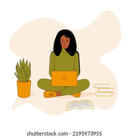 A dark-skinned girl with black hair in a green sweater and green pants, orange sneakers, sits on the floor with an orange laptop, next to a flower in an orange pot and books. Online training, work.