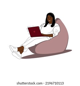 A dark-skinned girl with black hair in a white sweater and white pants, white sneakers, sits with a red laptop in a bean bag, next to a flower. Work online. Online education.