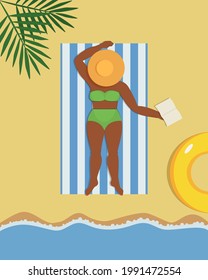 A dark-skinned girl in a green swimsuit and hat lies on the beach next to the sea under the leaves of a tropical tree with a book in her hand