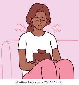Mulher de pele escura senta-se com almofada de aquecimento no estômago e expressão de dor. Ela sofre de cólicas menstruais e forte desconforto durante o período