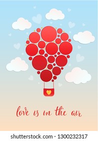 Decorated air balloon with red circles on sky background with clouds and hand lettering text Love is in the air. For greeting card, postcard, banner, poster, love concept, gift voucher, invitation.