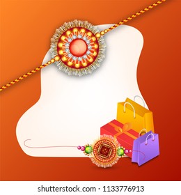 Decorated rakhi with gift box and shopping bag on shiny orange background with space for your message.