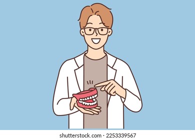 The dentist shows the model of the jaw. A young dentist intern holds a model of a dental jaw in his hands. The concept of dentistry. Vector illustration of the design.