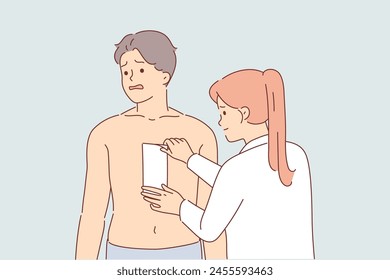 Depilation of hair on chest of man, experiencing pain from tearing wax tape, stands next to woman cosmetologist. Depilation causes fear and suffering in guy wants to become handsome svg