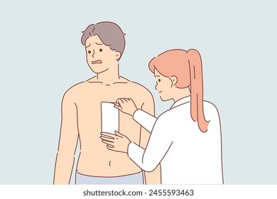 Depilation of hair on chest of man, experiencing pain from tearing wax tape, stands next to woman cosmetologist. Depilation causes fear and suffering in guy wants to become handsome