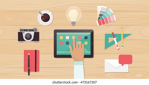 Designer desktop with camera, swatches and work tools, a designer is using apps on a touch screen tablet