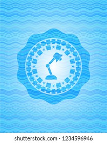 desk lamp icon inside sky blue water wave badge background.