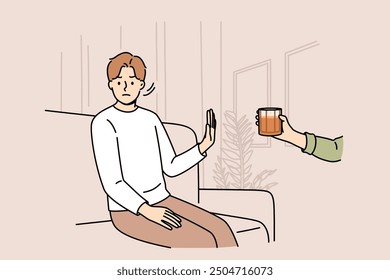 Determined man refuses alcohol, demonstrates stop gesture, sitting on sofa near hand with whiskey. Guy says no to alcohol and wants to live sober lifestyle to avoid hangover and intoxication