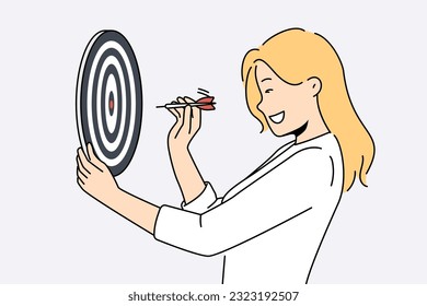 Determined woman throws darts at target for concept of business success and achieving set goals. Goal oriented businesswoman with darts board smiling setting and achieving ambitious goals