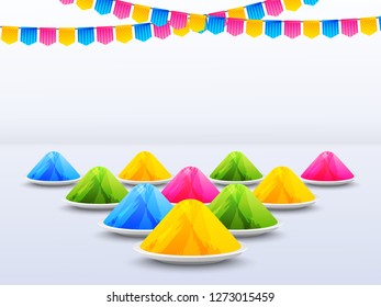 Different color bowl on glossy white background decorated with party flags for holi festival concept.