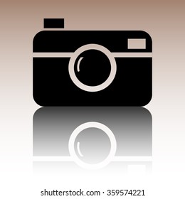 Digital photo camera icon. Black vector illustration with reflection.