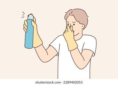 Dissatisfied man with aromatic spray to remove unpleasant odors covers nose with hand while spraying freshener. Householder guy uses air freshener to mask smell in unventilated room 