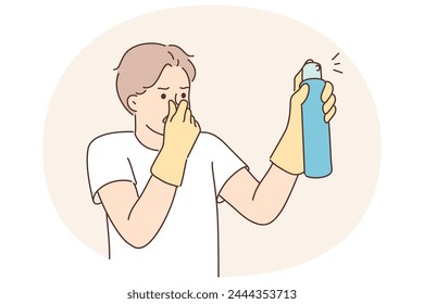 Dissatisfied man with aromatic spray to remove unpleasant odors covers nose with hand while spraying freshener. Householder guy uses air freshener to mask smell in unventilated room