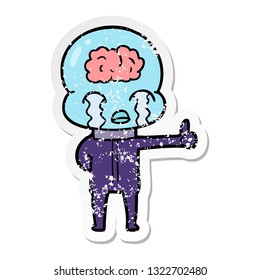 distressed sticker of a cartoon big brain alien crying but giving thumbs up symbol