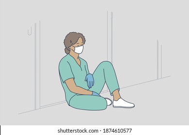 Doctor Burnout, Stress, Hard Conditions During Pandemic Concept. Tired Exhausted Black Female Nurse Or Doctor Wearing Protective Face Mask, Gloves And Blue Uniform Sitting On Hospital Floor