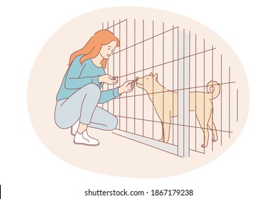 Dogs from shelter, volunteering, helping animals concept. Young happy girl cartoon character sitting and giving snack to dog in cage in shelter vector illustration 