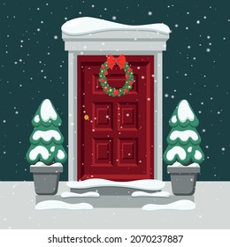 Door with a Christmas wreath. Christmas trees in the snow. Snow falls.