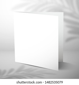 A double blank closed card stands near a white wall with a shadow of a palm tree. Mockup for design