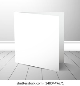 A double blank closed card stands near a white wall on plank floor. Mockup for design