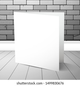 A double white blank closed card stands near a brick wall on plank floor. Mockup for design