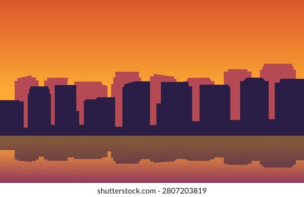 A dramatic vector graphic featuring dark violet city buildings silhouetted against a brilliant, fiery orange and yellow gradient sunset sky. The warm, intense light of the evening cast creates a beautiful contrasting dark reflection across the smooth water surface.