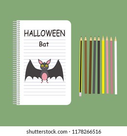 Drawing of a bat with open wings in a school notebook, as a symbol of Halloween, along with the pencils used to color it.