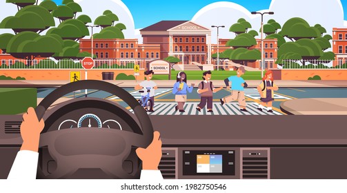driver holding the steering wheel and waiting schoolchildren crossing road on crosswalk near school building road safety