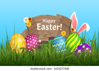 Ears of an Easter bunnyabove the grass and flowers, blue nature background with wooden board lettering Happy Easter