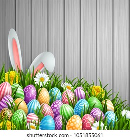 Easter background with bunny ears, flowers and colored decorated eggs in the grass on a wood background