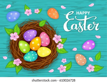 Easter bird nest with decorated eggs with spring flowers on blue wooden table, hand lettering