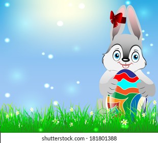 Easter bunny holding Easter egg against a background of blue sky and green grass