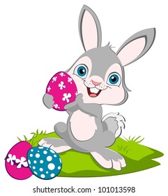 Easter Bunny holding a pink egg and smiling, two eggs on the ground.