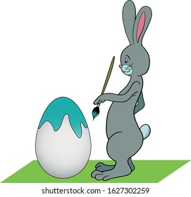 Easter bunny paints an egg with a brush