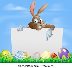 Easter bunny pointing at blank sign with painted chocolate Easter eggs in green field