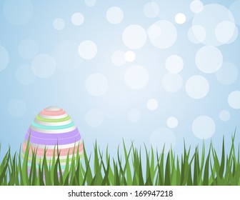 Easter egg with colorful stripes sitting in grass with a bokeh sky background
