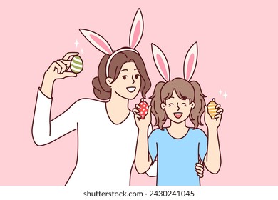 Easter eggs in hands of happy mother and daughter with bunny ears, to celebrate traditional christian holiday. Easter portrait of little girl with nanny or older sister rejoicing in coming of spring