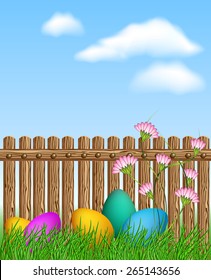 Easter eggs lying in the grass in front of a wooden fence