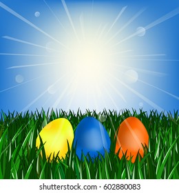 Easter eggs on the green grass against the blue sky with the sun